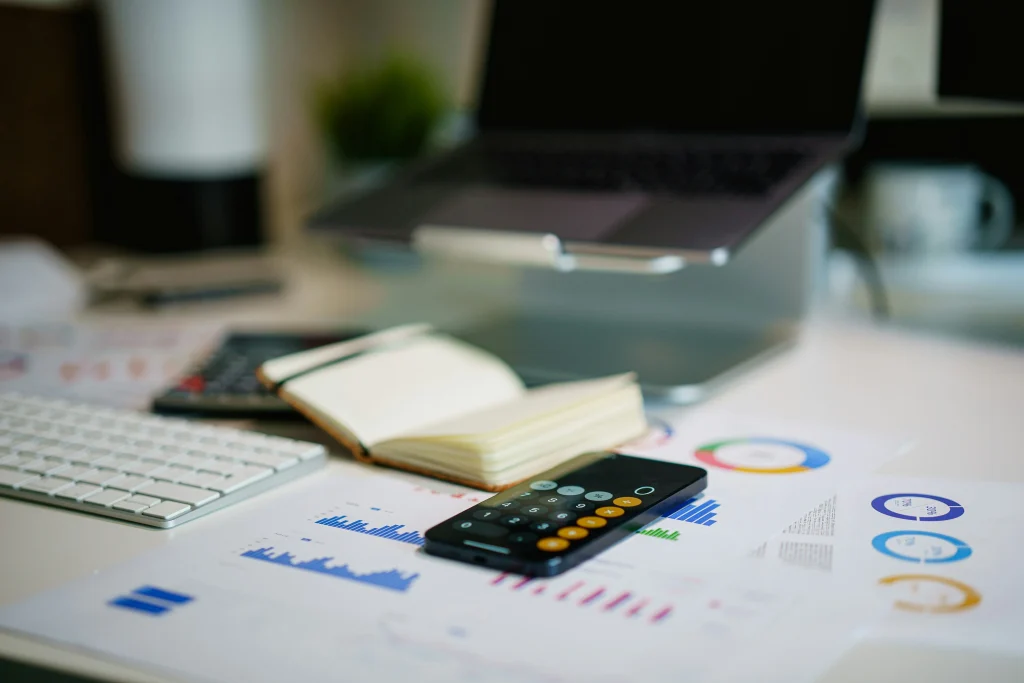 Laptop, notebook and calculator with business charts on a desk